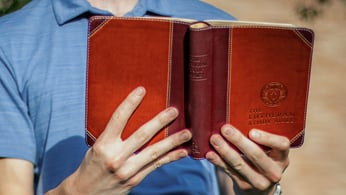 Someone in a blue shirt holding an open Bible