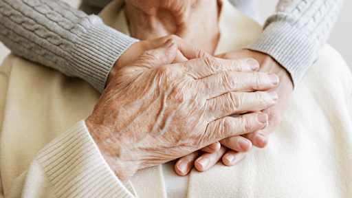 A older woman's hand being held gently by a friend