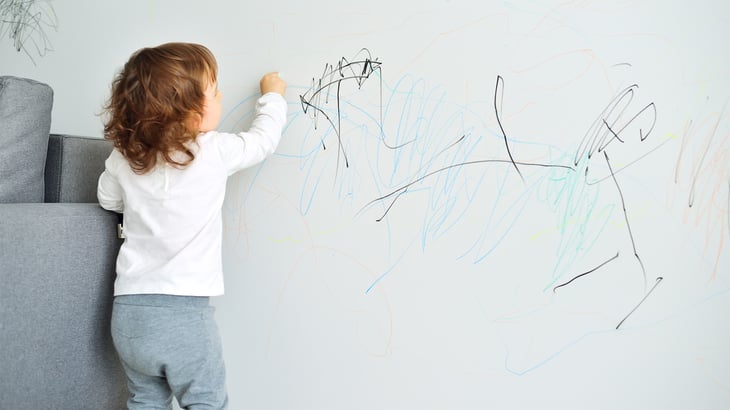 Small child coloring on wall with marker