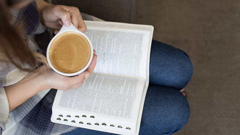 woman-with-bible-open-on-lap-and-holding-a-cup-of-coffee