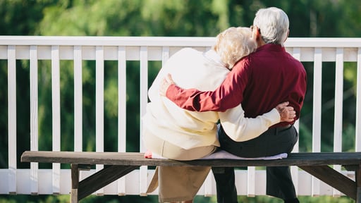Sweet elderly couple sits together on a park bench in an embrace