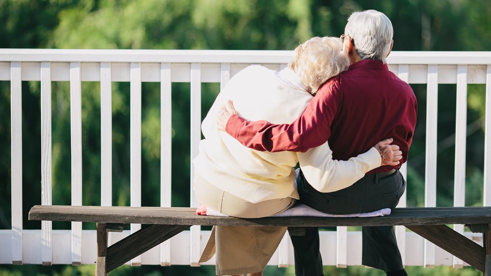 Sweet elderly couple sits together on a park bench in an embrace