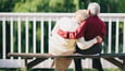 Sweet elderly couple sits together on a park bench in an embrace