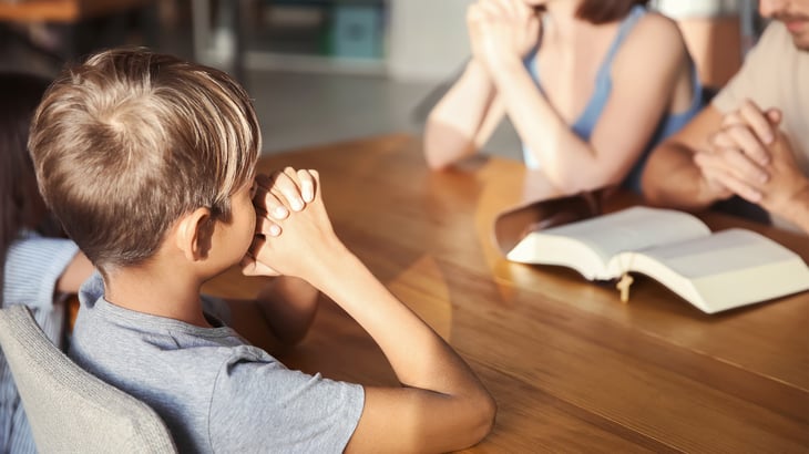 Little boy with hands folded prays with family at table