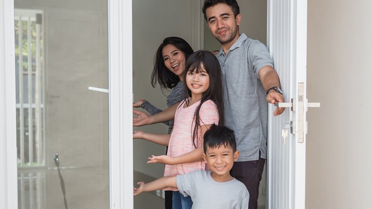 A family of four warmly welcomes guests inside their front door