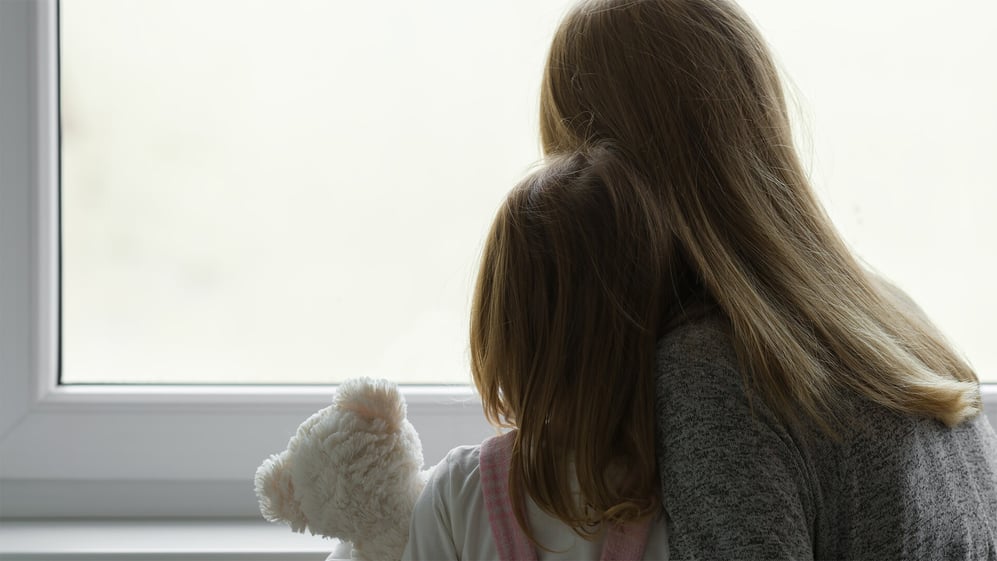Mother and daughter embrace while looking out window 