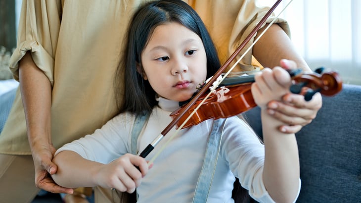 A young girl being taught to play violin. 
