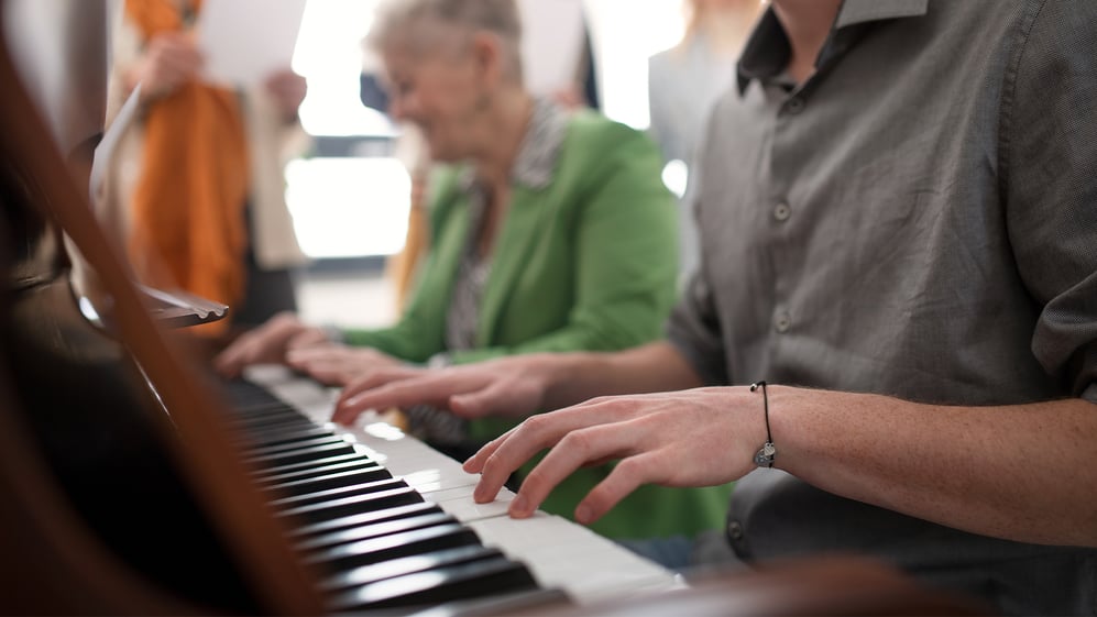 A young man and elderly woman playing piano together