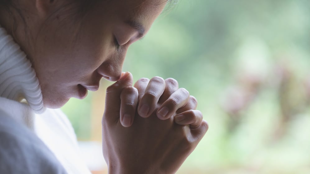A young woman bows her head to pray.